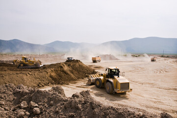 Earthworks in an open area on a summer sunny day. Cargo dump trucks, excavators, wheel loaders and bulldozers operate at the same time.
