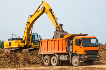 Excavator loads clay into the body of a dump truck on a sunny summer day