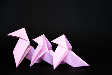 Three pink origami birds on a black background