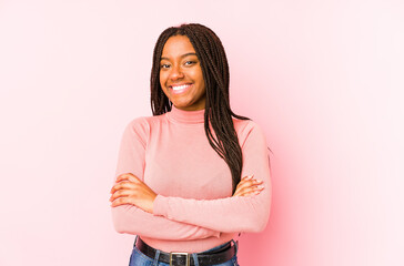 Young african american woman isolated on a pink background who feels confident, crossing arms with determination.