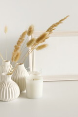 Photo frame mock up, fluffy reeds bouquet in a vase, interiour accessories near the white wall. Copy space template. Minimalist scandinavian interior design .