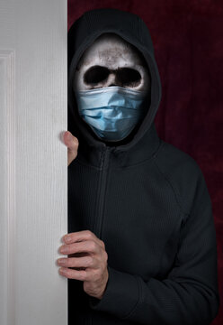 Stalker or burglar entering a home through doorway with wearing a human skull fitted with medical face mask against coronavirus pandemic