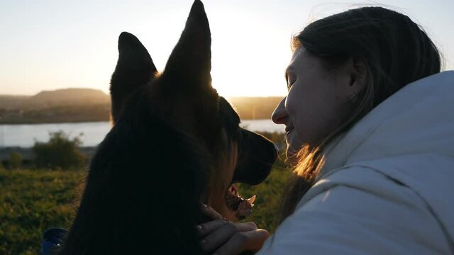 Young woman and her pet dog german shepherd watch the sunset by the river