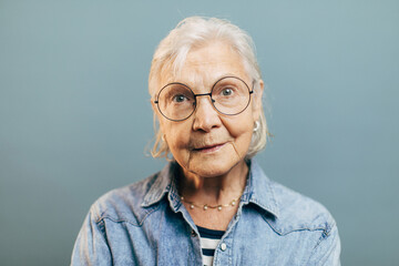 Wise concentrated old woman with attentive gray eyes in big round glasses looks into camera....