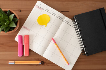 Top view. Back to school or work from home space. Stationery. Blank calendar, black notebook, color markers, plant.