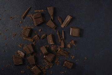 Dark chocolate broken into pieces isolated on a dark background. Top view, flat lay. Free space for text.