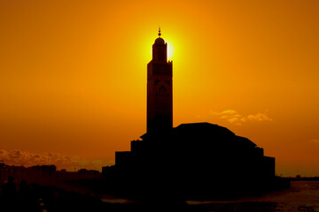 Orange sunset above the Black silhouettes by minaret of the mosque of Hassan II Mosque in Casablanca, Morocco. Muslim evening prayer time