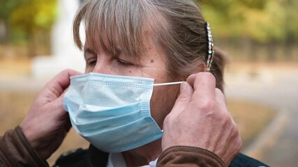 Senior caucasian man helps puts a medical mask on the face of an senior woman - Powered by Adobe