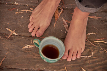Women's bare feet stand on a wooden floor covered with autumn leaves.