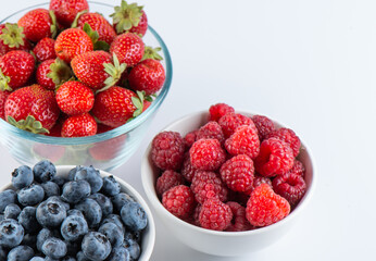 Fresh berries raspberries, strawberries and blueberries in bowls isolated on white background, top view