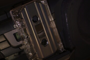 Audio cassette - in a dark light, against the background of a tape recorder.