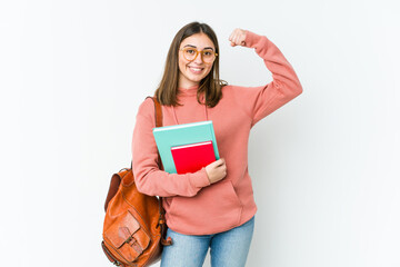 Young student woman isolated on white bakcground showing strength gesture with arms, symbol of...
