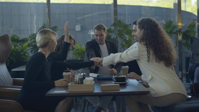 Cheerful colleagues putting hands on top of each other and hugging. Five happy coworkers celebrating successful business deal. Teamwork and partnership.
