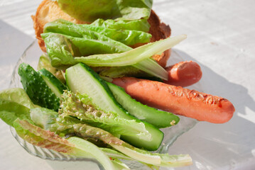 sausages, cucumbers and greens on a transparent plate