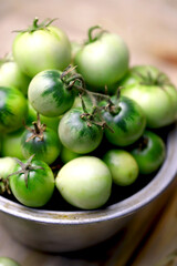Green tomatoes in a bowl on a wooden surface. Rustic style. Selective focus. Macro.