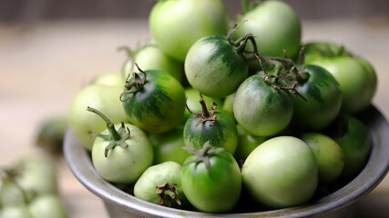 Green tomatoes in a bowl on a wooden surface. Rustic style. Selective focus. Macro.