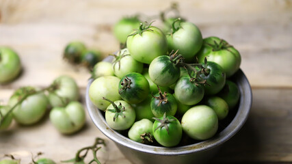 Green tomatoes in a bowl on a wooden surface. Rustic style. Selective focus. Macro.