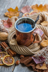 Copper mug with hot tea on a wooden table with autumn leaves. Retro style photo