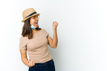 Obraz na płótnie Canvas Young latin woman wearing hat and mask to protect from covid isolated on white background raising fist after a victory, winner concept.