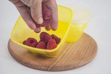 Woman's hand puts raspberries in a plastic box. Cooking vitamin food for lunch