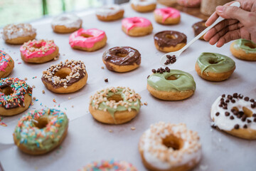 close up of chef's hand decorating various donuts with chocolate frosted, pink glazed and donut sprinkles