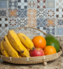 Brazilian dining table with bananas, apples, orange and avocado in the straw bowl and also with sugar, coffee and condiments. Typical Brazilian cuisine with tiles decorated in the background.