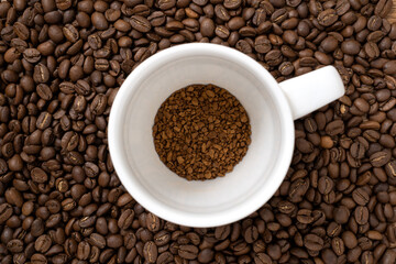 Cup with a portion  of instant coffee on coffee beans background. Concept of natural coffee in granules.