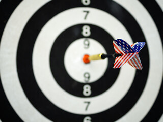 Dart arrow with tail of USA flag backgroun hitting in the target center of dartboard. Bullseye is a...