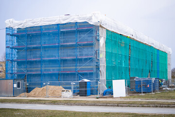 The restoration process of an old apartment building. The object is covered with a protective net. Near building material and supporting structures. Housing recovery concept. Close-up.