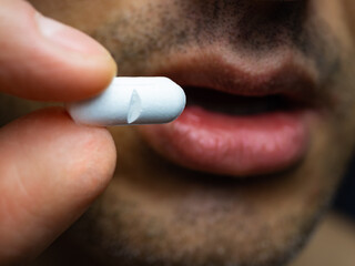 A tanned man holds a pill in his hand to put it in his mouth and swallow it. A white capsule or tablet as an aid for illness. The concept of a healthy lifestyle and health care. Close-up.
