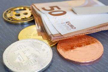 Close-up of bundle of 50 euro bills banknotes on a golden, silver and bronze bitcoin coin on a gray wooden texture table background. Conceptual image for crypto currency - BTC.