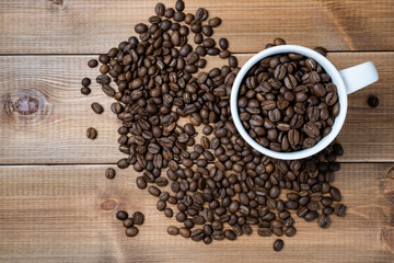 White ceramic cup full of coffee beans on wooden table.