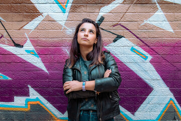 Young woman posing thoughtful in front of colourful graffiti street wall  © Fred