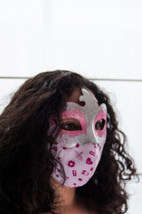 Curly girl wearing pink mask at home with a window at background 