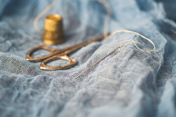 Closeup of Needle and Thread on Blue Fabric with Vintage Scissors and Thimble in Background