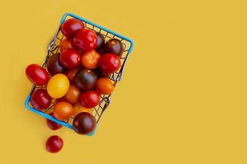 supermarket shopper basket filled with vegetables. shopping cart. Ripetasty delicious red vitamin cherry tomatoes. Yellow background place for text copyspace banner. Vegan food healthy fresh eating 