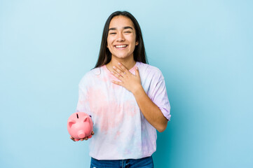 Young asian woman holding a pink bank over isolated background laughs out loudly keeping hand on chest.