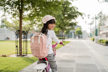 a portrait of a cheerful and happy little girl riding a bicycle in the park going to school by herself