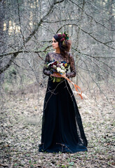 A Gothic woman in a black dress with a bouquet of flowers in a mysterious forest. Halloween concept.