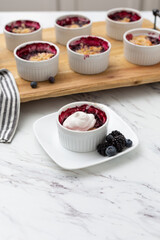 White Ramekins of Blueberry and Blackberry Cobbler on a Wooden Tray; One Isolated in Front; Kitchen Countertop