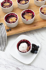 White Ramekins of Blueberry and Blackberry Cobbler on a Wooden Tray; One Isolated in Front; Kitchen Countertop