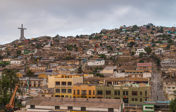 Coquimbo, Chile - December 7, 2008: Hill completely covered with houses in different colors under brown cloudscape. Millennium Trinity Cross on side.