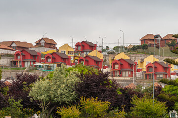 La Serena, Chile - December 7, 2008: Group of red and yellow identical houses in neighborhood under silver sky. Green foliage up front.