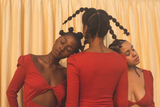 Two Black models with eyes closed heads resting on shoulder of third model