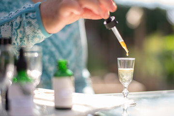 woman using dropper to add a tincture to a shot glass of water