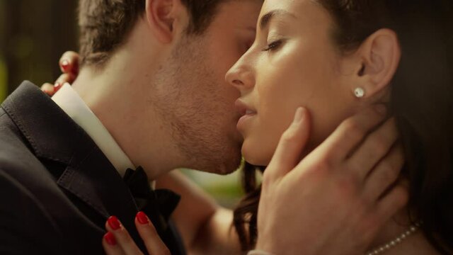 Handsome man kissing woman cheek outdoors. Sensual couple posing in park