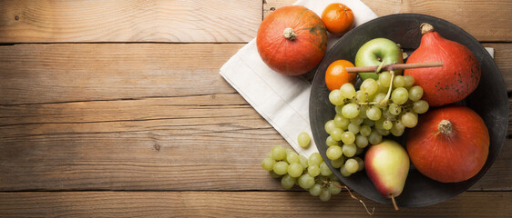 Hokkaido Red cury Pumpkins, grapes and other autumn fruits in old pewter plate on wooden background, top view.