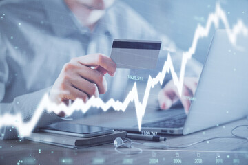 Double exposure of man hands holding a credit card and Forex graph drawing. Stock trading and digital fintech in Internet E-commerce concept.