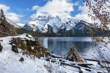Snowy Hiking Trail and Wooden Indian Teepee or Tipi Structure with sweeping landscape View across Lake Minnewanka to Rugged Fairholme Range Canadian Rocky Mountain Peaks in Banff National Park