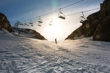 A man skiing down a slope passing under a ski lift in backlit